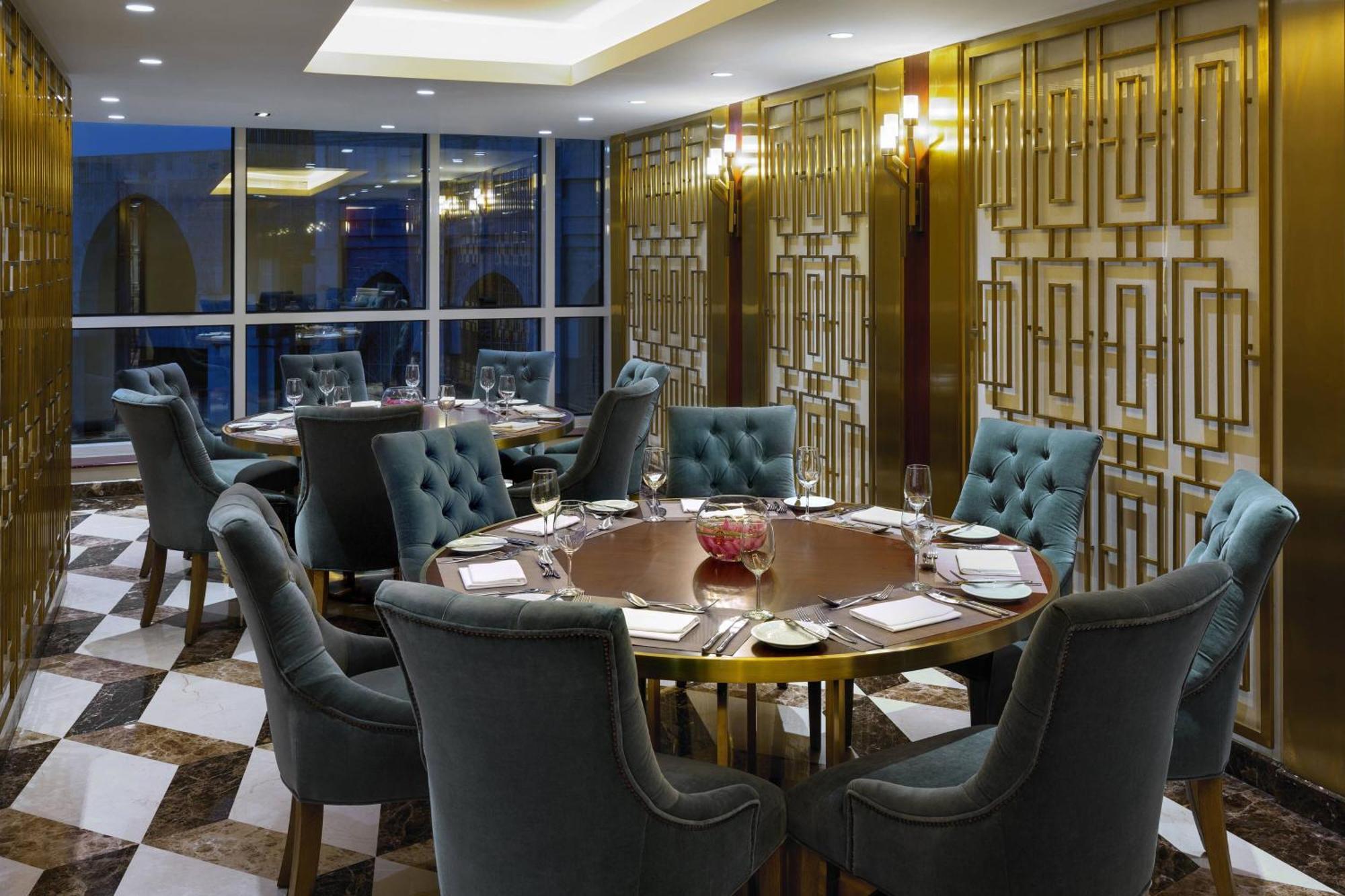 Sheraton Makkah Jabal Al Kaaba Hotel Mekka Kültér fotó The photo shows an elegant dining room with a sophisticated ambiance. It features a round wooden table at the center, surrounded by plush chairs upholstered in a soft, teal fabric. The room has a stylish décor, highlighted by a geometrically patterne