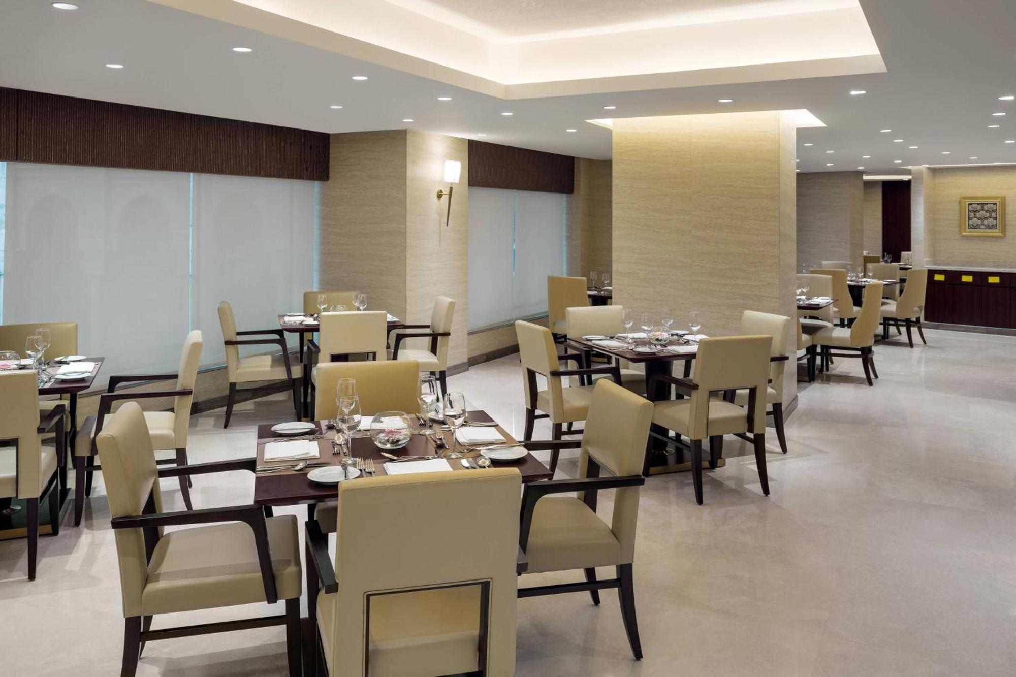 Sheraton Makkah Jabal Al Kaaba Hotel Mekka Kültér fotó The photo shows a modern restaurant interior. It features several dining tables, each set with utensils and tableware. The chairs are upholstered in a light fabric, and the overall decor is sleek and minimalistic, with soft lighting from overhead fix